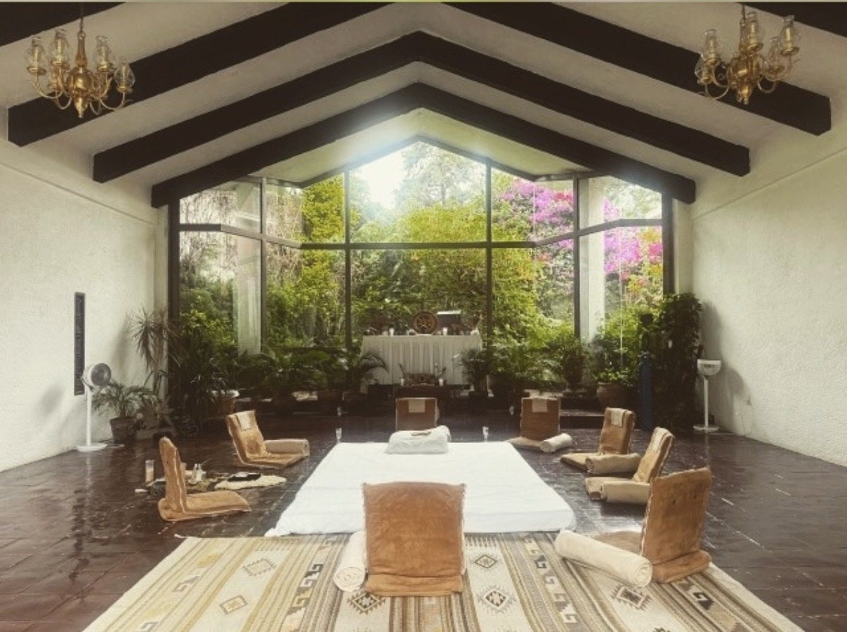 A high-ceilinged room at Tandava set out for a ceremony, cushions and a mat facing tall windows onto a garden